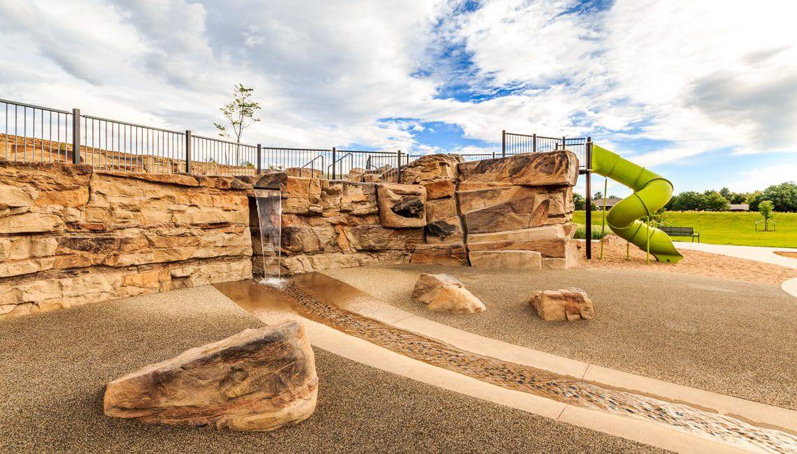 Park with rockwork and stream bed next to playground.